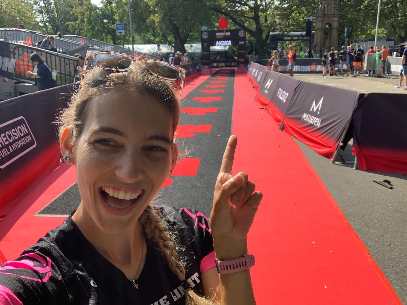 A woman smiles at the camera pointing up at a finish line mark.