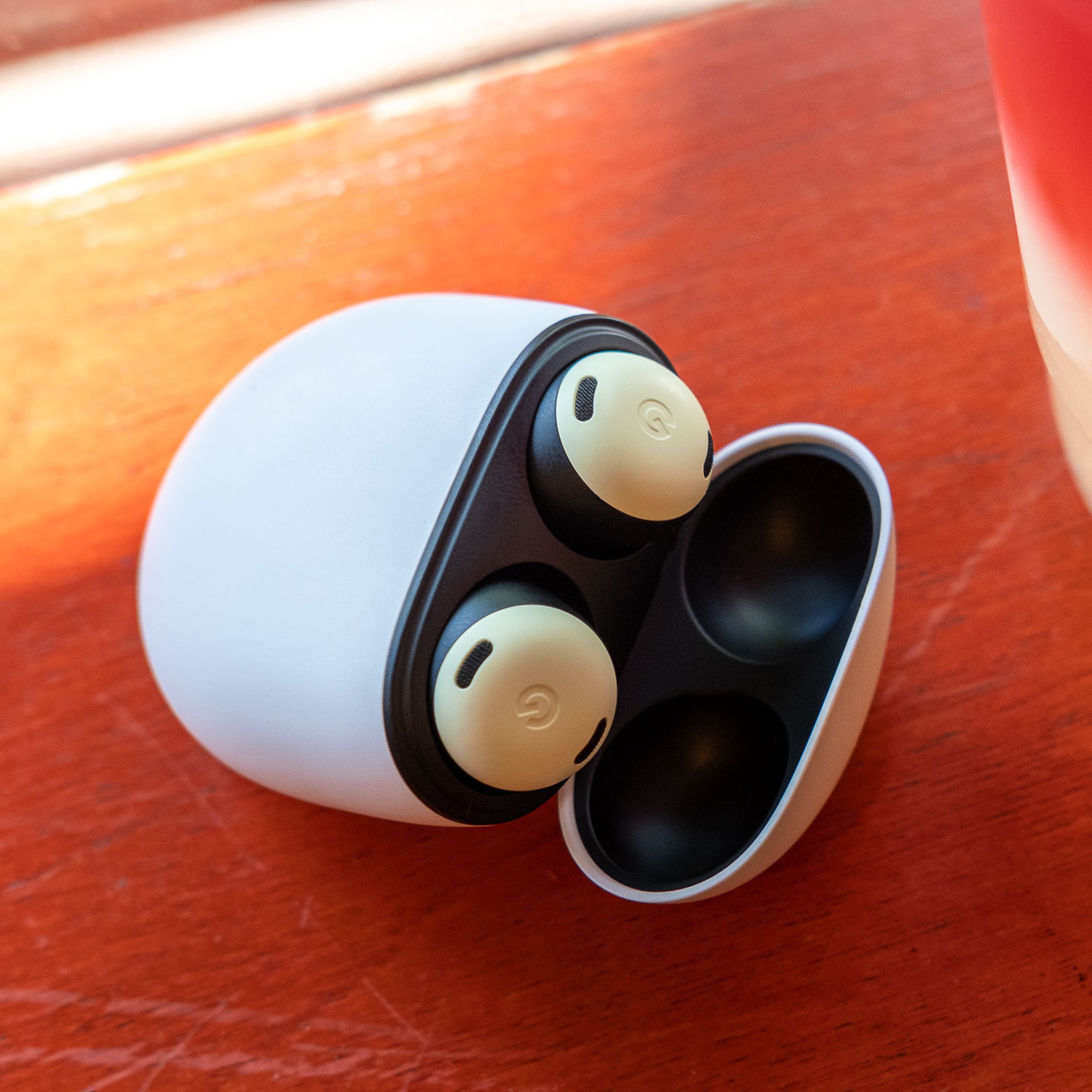 The yellow Pixel Buds Pro wireless earbuds sitting in their charging case with the lid open, resting on an orange table beside a plastic cup of colorful lemonade.