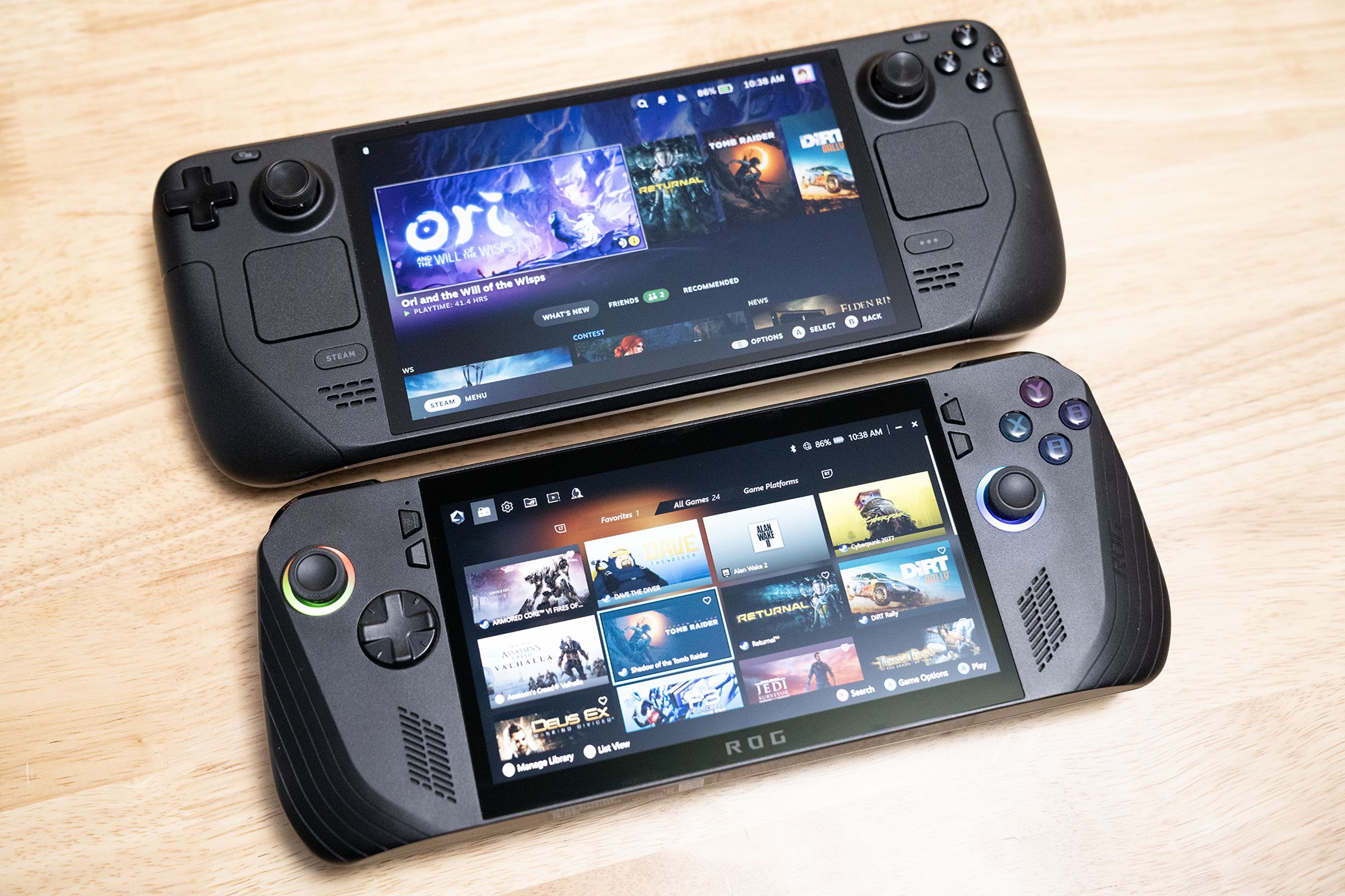 The Steam Deck sitting directly above the ROG Ally X on a table, showing how the two black-colored handhelds are quite similar in size and shape, though they diverge in control layouts.