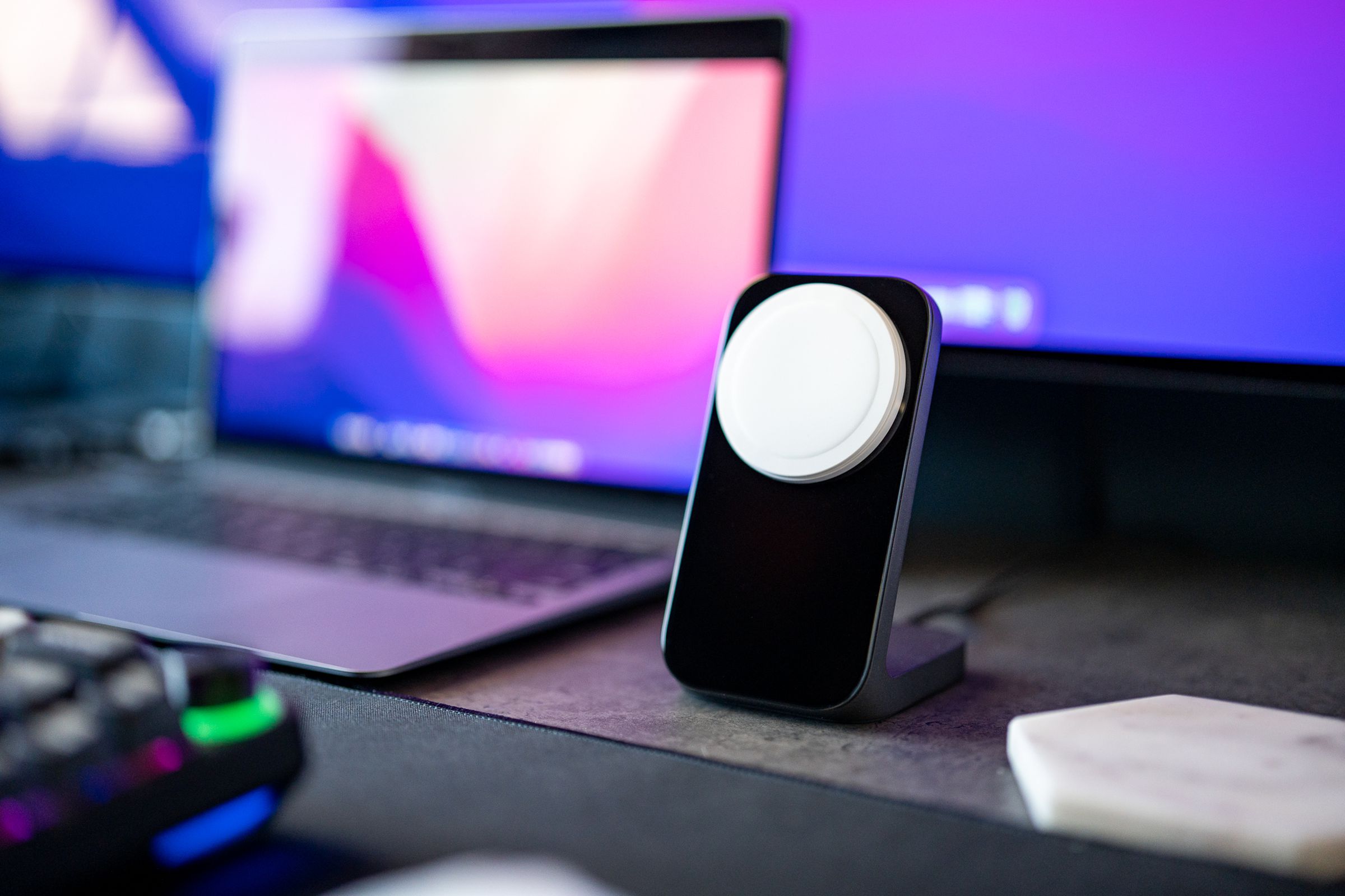 The Nomad Stand One MagSafe charger in black, sitting on a gray desk beside a MacBook Air, keyboard, and monitor.