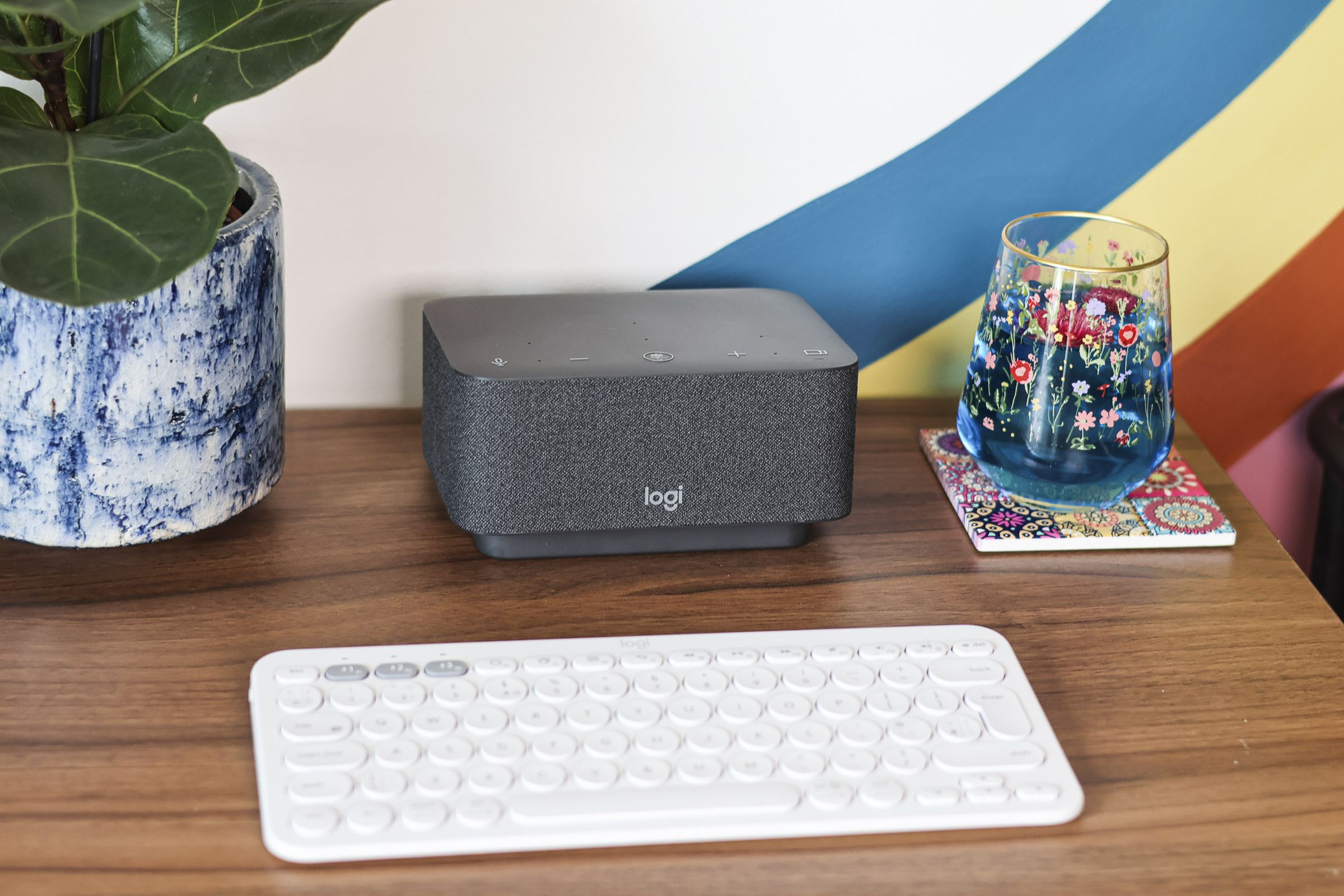 A photograph of the Logitech Logi Dock on a desk, beside a blue drink, a house plant, and a Logitech keyboard