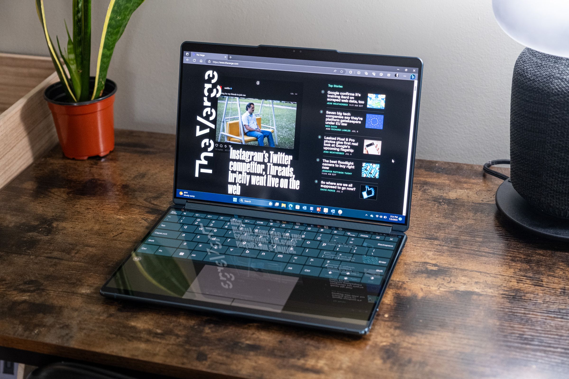 A Lenovo Yoga Book 9i in clamshell mode on a wooden desk.