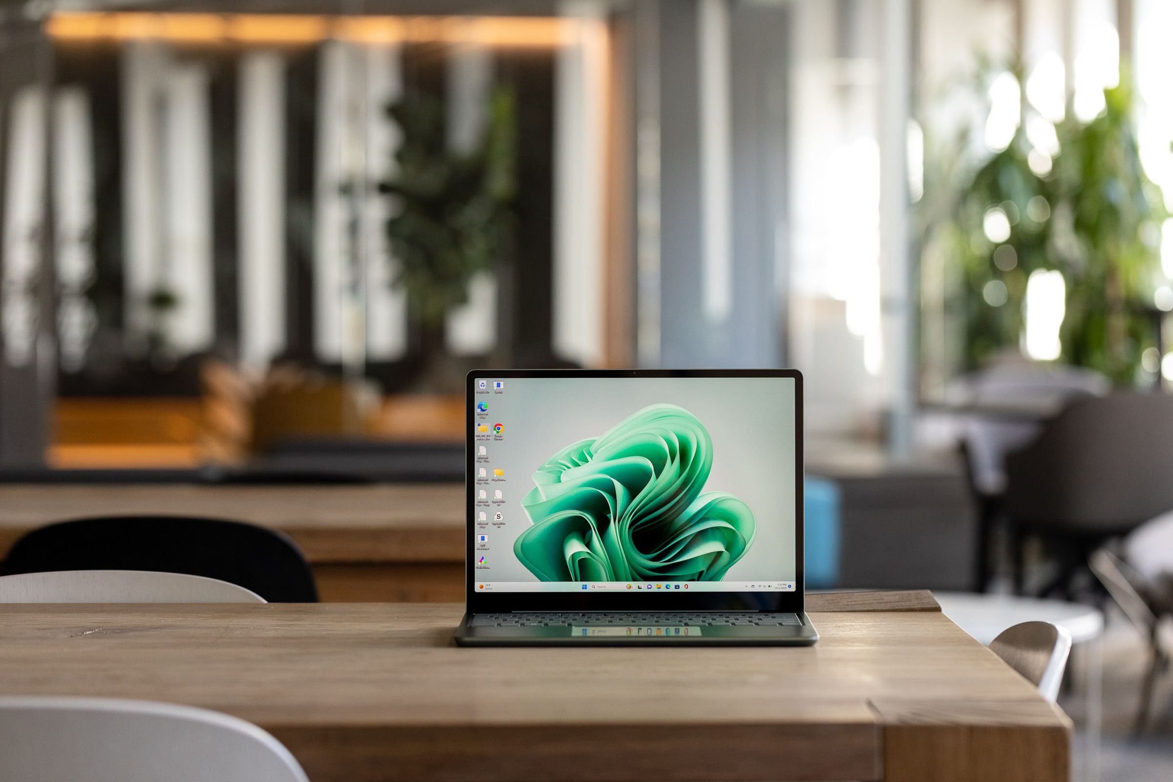 The Microsoft Surface Laptop Go 3 displaying a green Windows desktop on a table in a cafe setting.