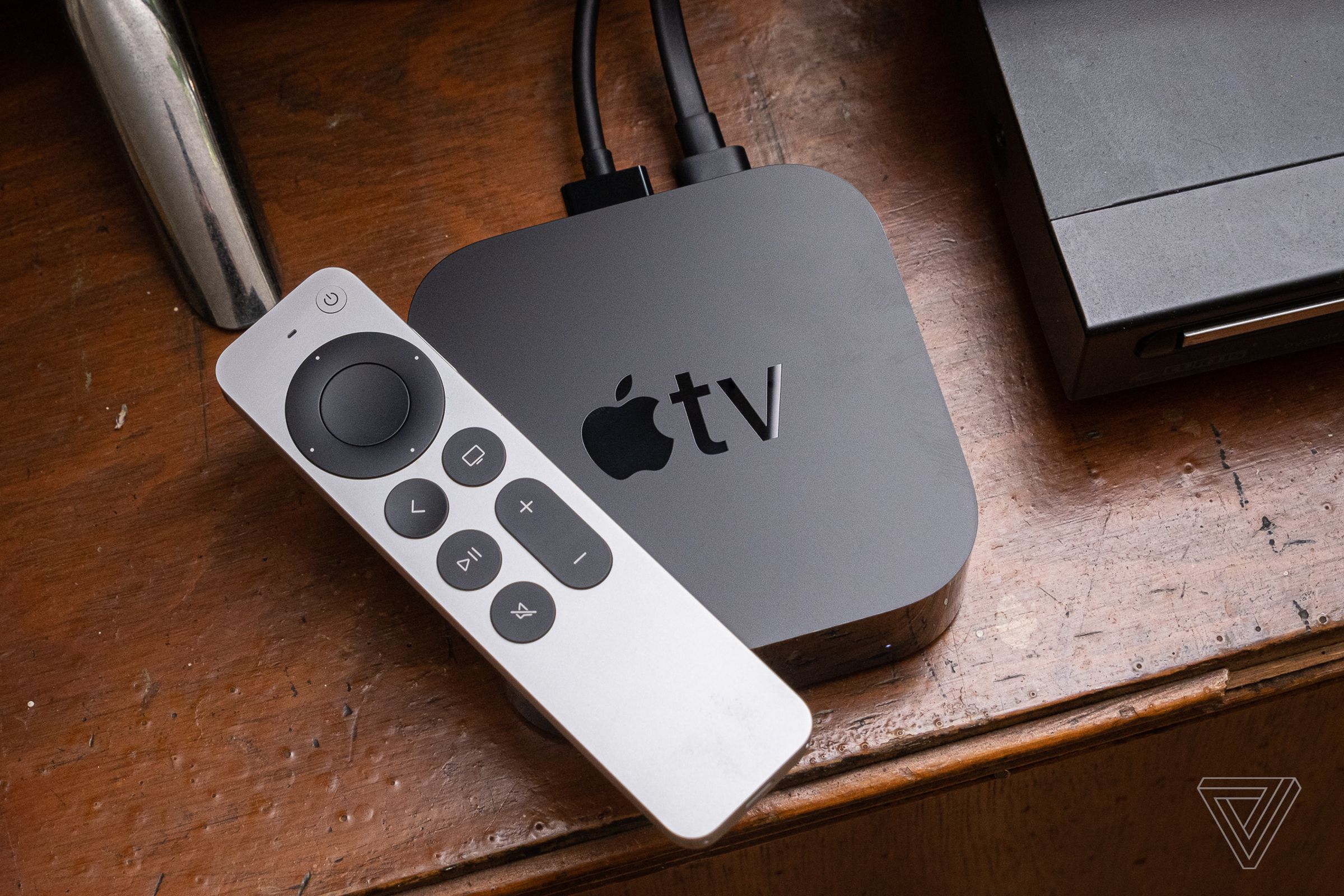 An Apple TV from 2021 and its Siri Remote sit on top of a wooden entertainment center.