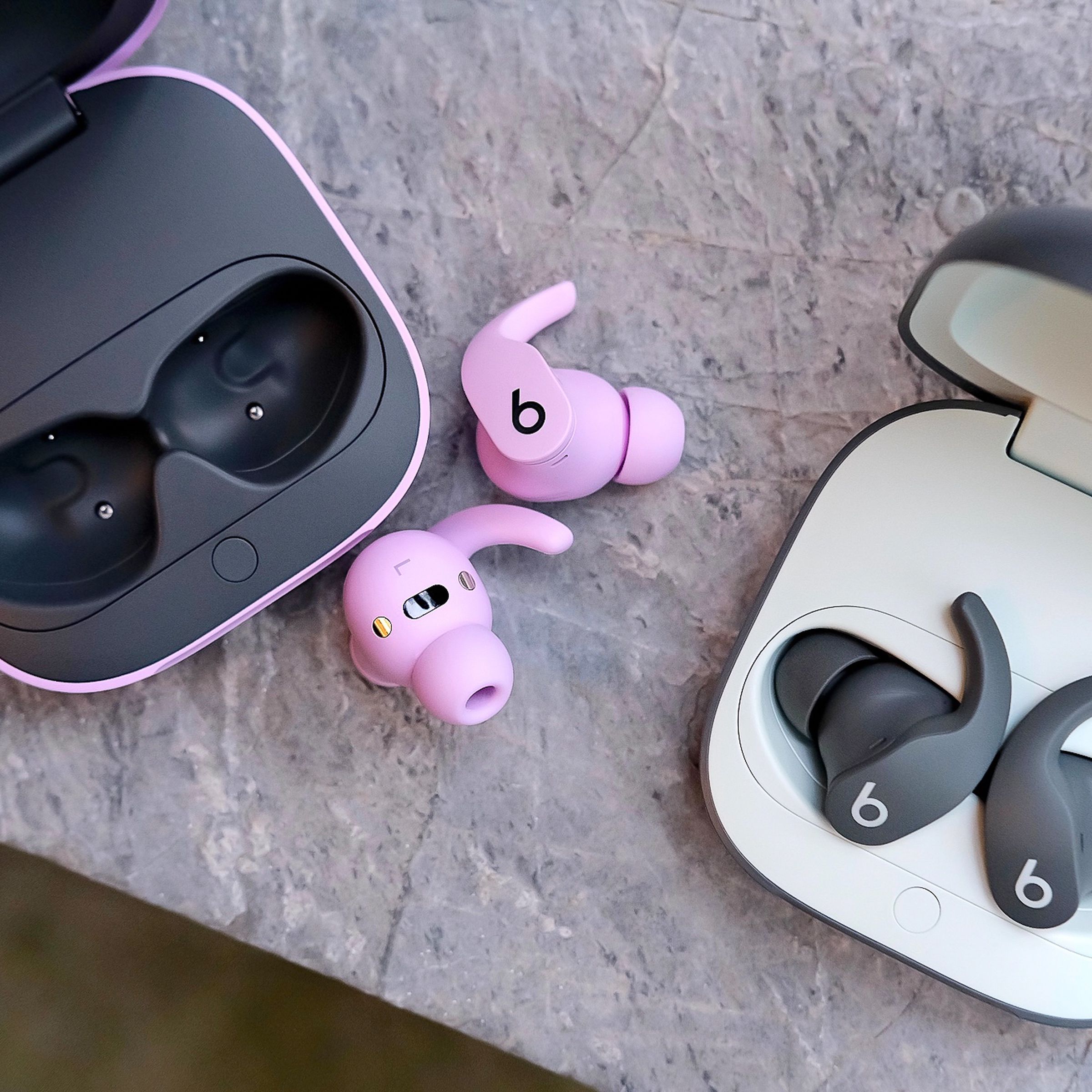 A photo of two pairs of Beats Fit Pro earbuds on a marble surface.