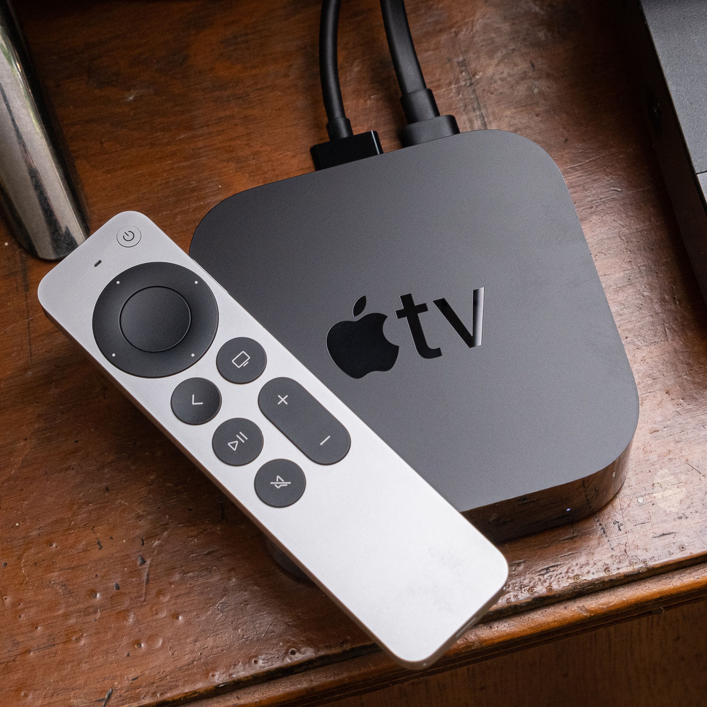 An Apple TV from 2021 and its Siri Remote sit on top of a wooden entertainment center.