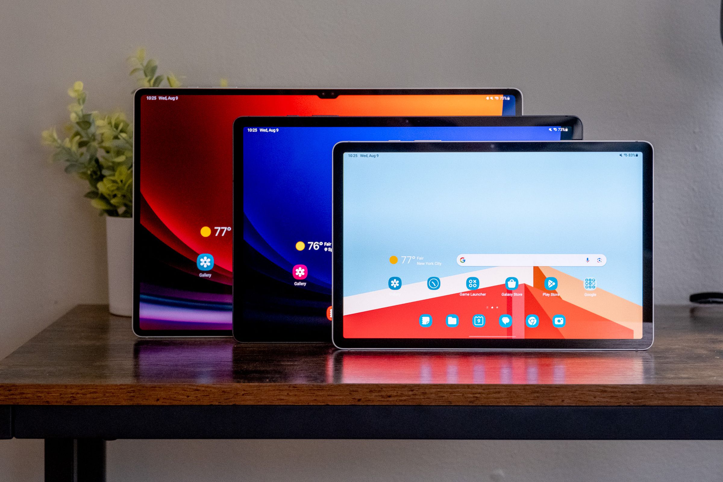 The Samsung Galaxy Tab S9, Tab S9 Plus, and Tab S9 Ultra standing in a line on a wooden desk.