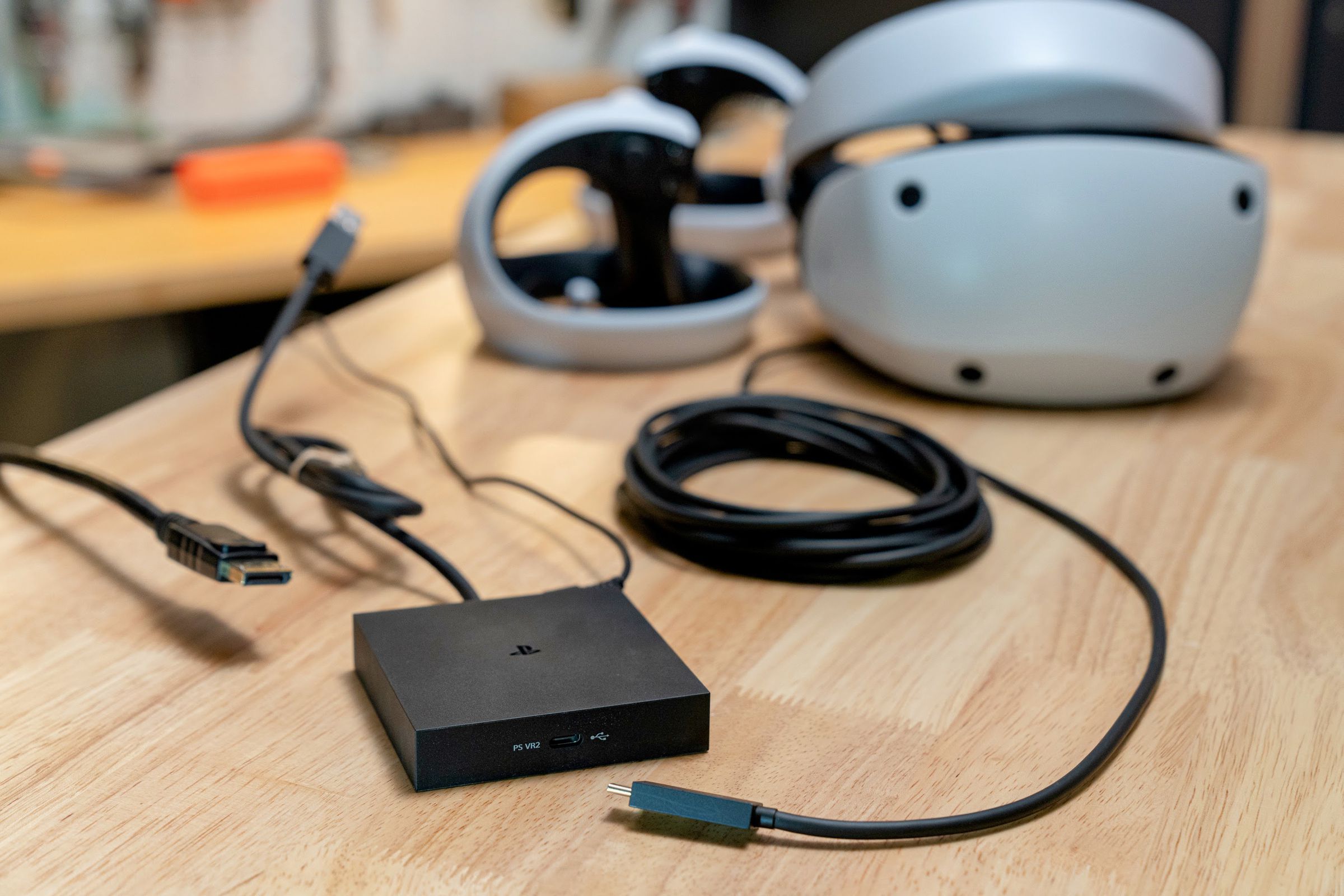 A black square puck, three inches by three inches, with various cables coming out of it, some floating in midair, and a PlayStation VR2 headset in back.