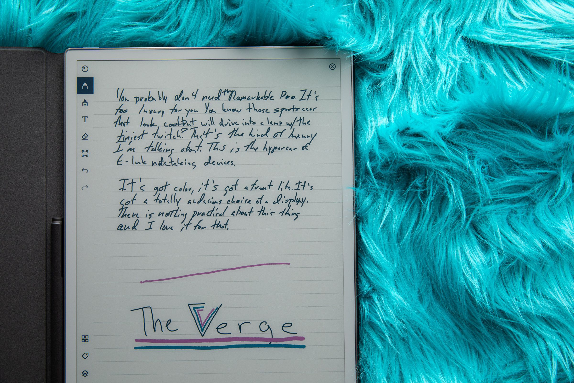 A picture of a color E Ink display resting on what might be the pelt of an electric-blue Wookiee. Handwritten notes in black “ink” cover the top half of the display, and a The Verge logo is drawn on the lower half, with a magenta line above it, the V in “Verge” done in three concentric V’s of black, pink, and blue, and “The Verge” underlined once in blue and once in magenta.