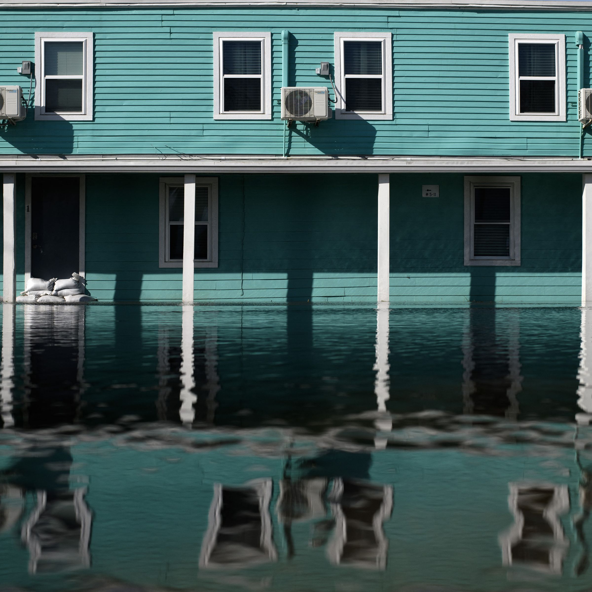 Air conditioning units amid a row of windows in a motel rising above floodwaters.