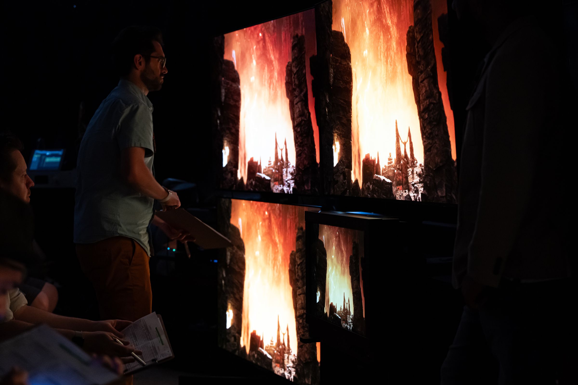 A man looks at several large TVs showing movie scene with bright flames