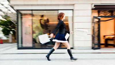 Women walking with a black dress and boots holding a white hand bag