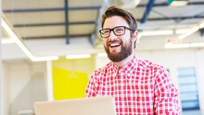 A bearded man holding a laptop wearing a longsleeve red checkered