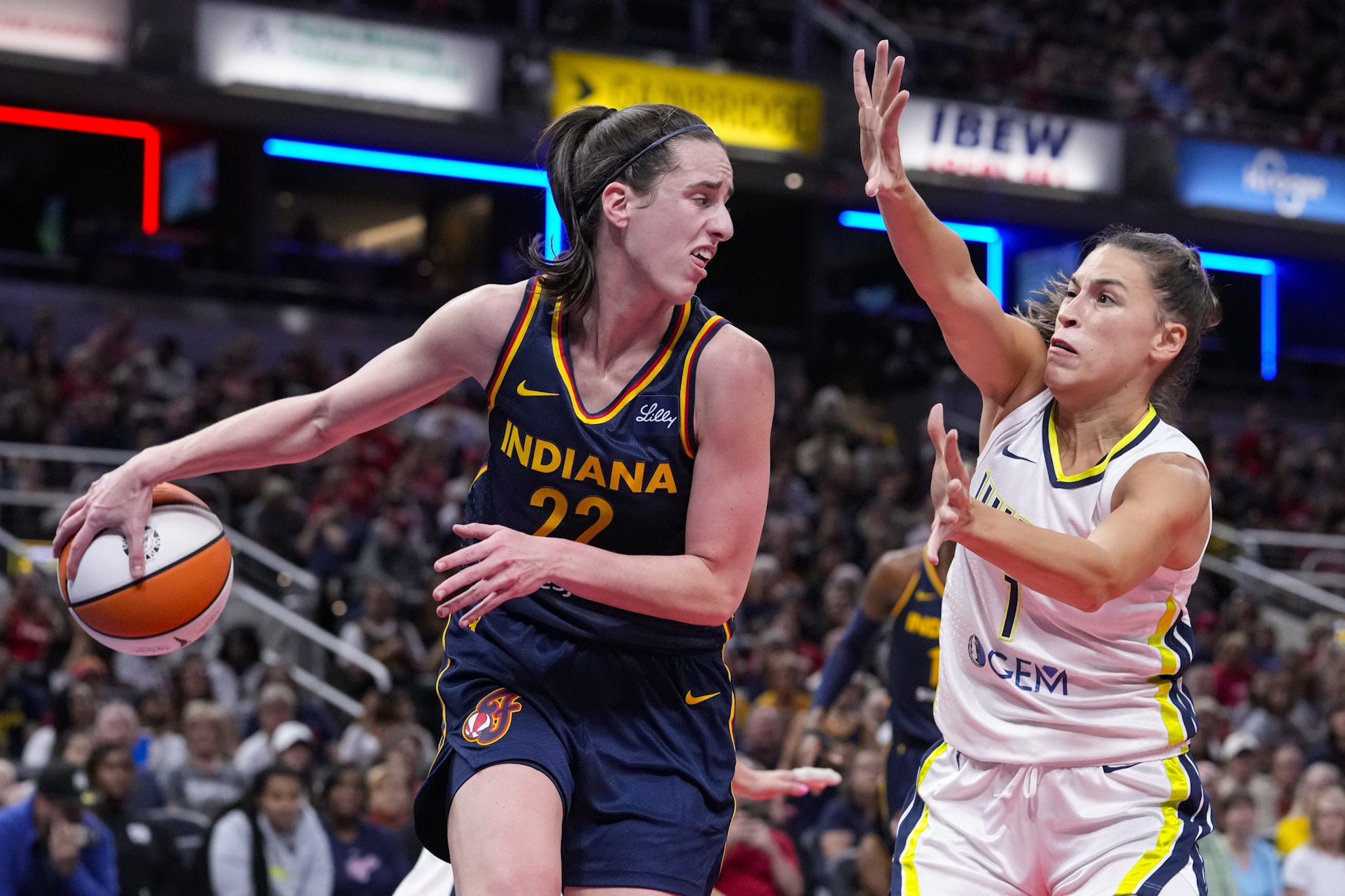 Indiana Fever guard Caitlin Clark makes a behind the back pass in front of Dallas Wings guard Sevgi Uzun.