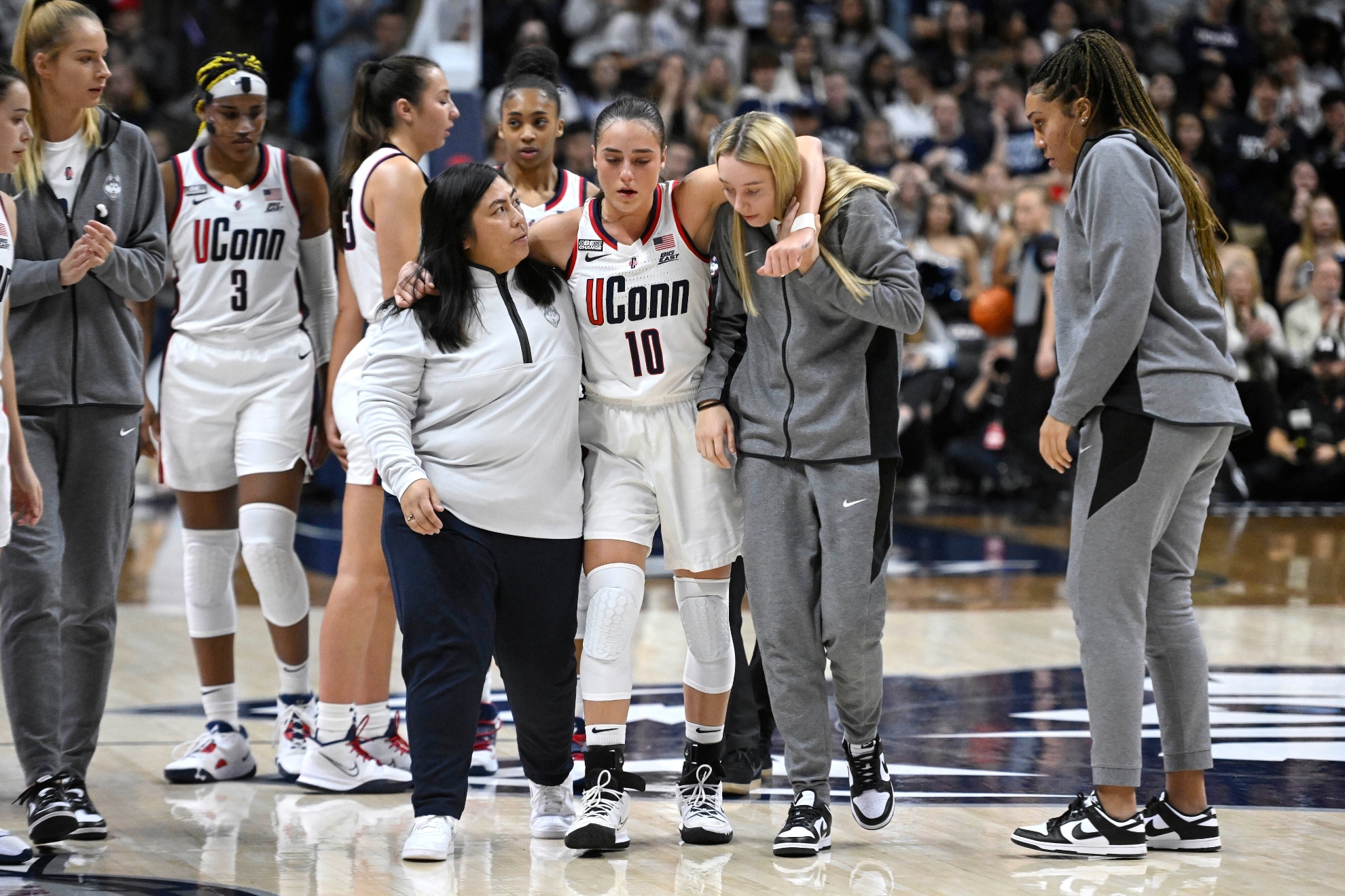 UConns Nika Muhl (10) is helped off the court by athletic trainer Janelle Francisco, left, and teammate Paige Bueckers, right, during the second half of an NCAA college basketball game against Princeton, Thursday, Dec. 8, 2022, in Storrs, Conn.