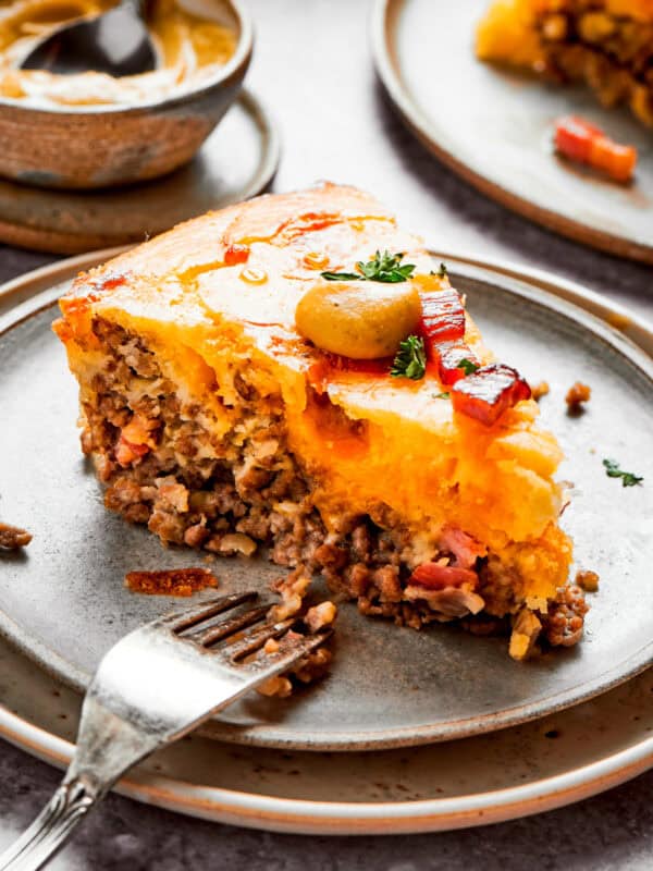 A slice of cheeseburger pie on a plate with a fork set near it.