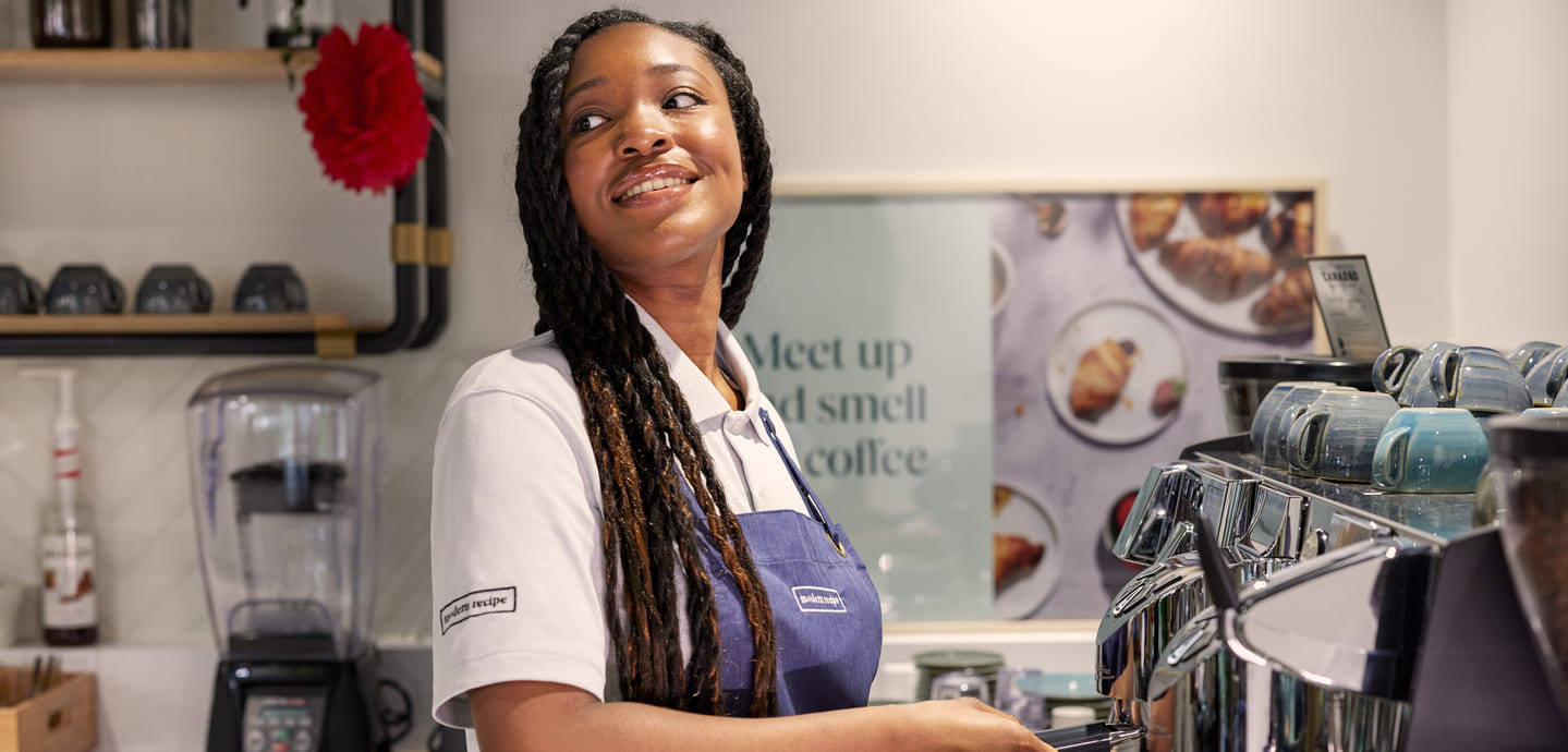 A smiling woman in an apron working in a coffee shop.