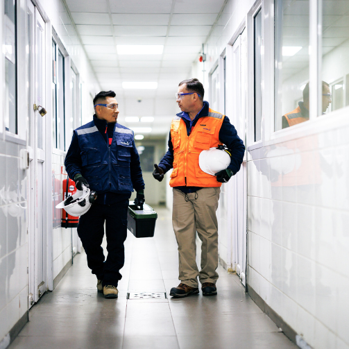 A man in an orange vest walking with a man holding a toolbox.