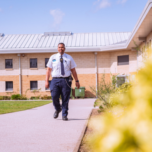 A man walking down a sidewalk in an open area, with a building in the background