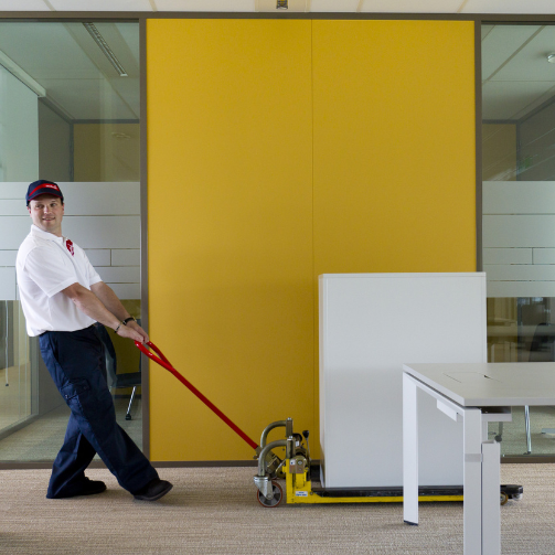 A man in a white shirt pulling a piece of equipment on a trolley.