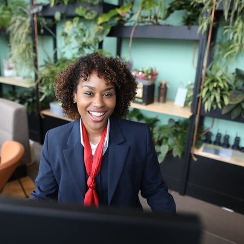 A professional woman in a business suit smiles while seated at a desk.