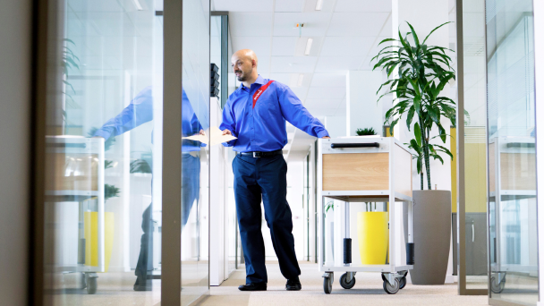 A man in a blue shirt standing in an office hallway with a cart