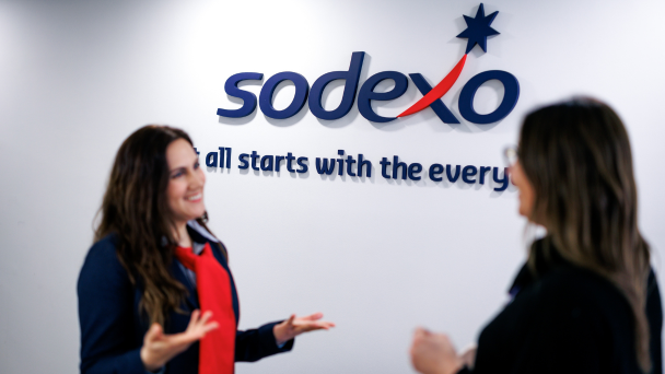 Two women conversing in front of a sign that reads "sodexo"