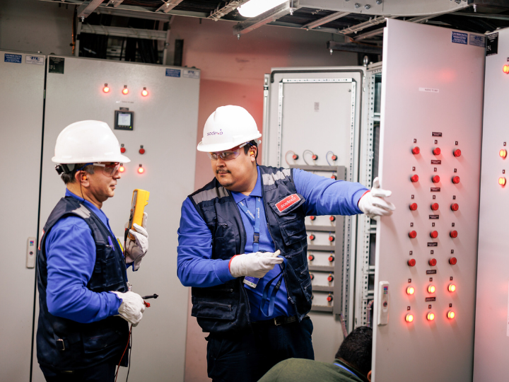 Two men wearing white hard hats, engaged in a mechanical project at a work site.