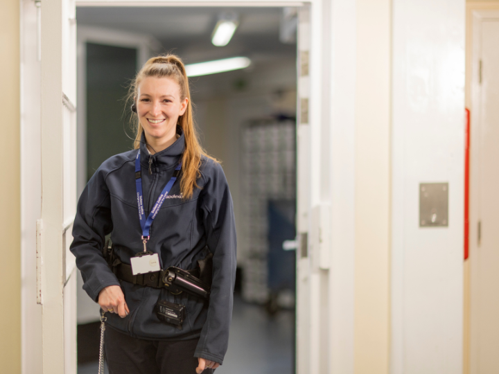 A woman in a dark blue jacket standing in an open doorway, smiling