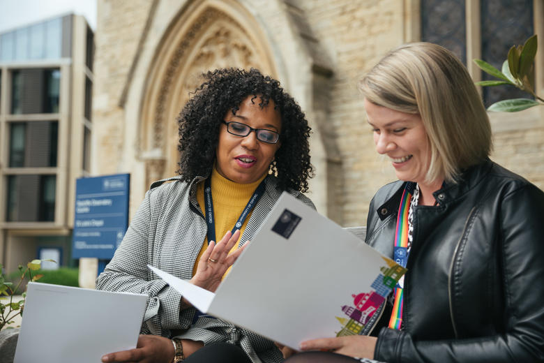 Two women looking at a brochure whilst sitting outside an Oxford University building 