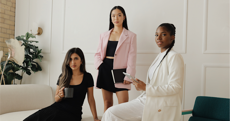 Three women wearing professional attire pose for a photo in a modern-looking workplace.