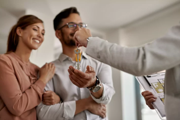 Casal feliz recebe chaves de imóvel de agente imobiliário.