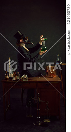 Plague doctor mixing his elements, experimenting and researching in vintage laboratory against dark mystery background. 121060720