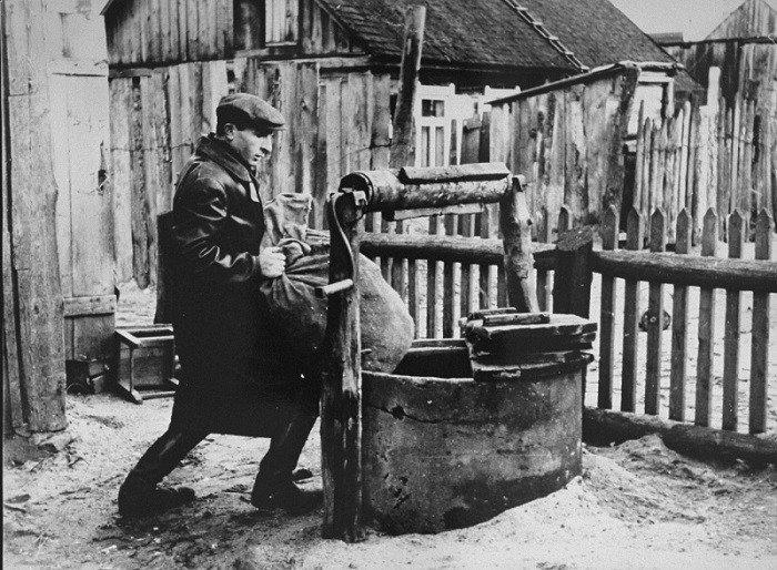 Photograph taken by George Kadish: a member of the Kovno ghetto underground hides supplies in a well used as the entrance to a hiding ...