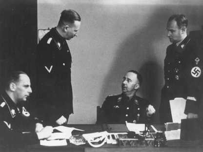 Heinrich Himmler (seated, center), chief of the SS, with Reinhard Heydrich (standing, left), chief of the Reich Main Security Office ...