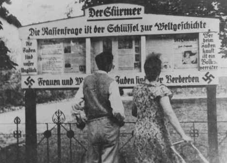 A German couple reads an outdoor display of the antisemitic newspaper "Der Stuermer" ("The Attacker").