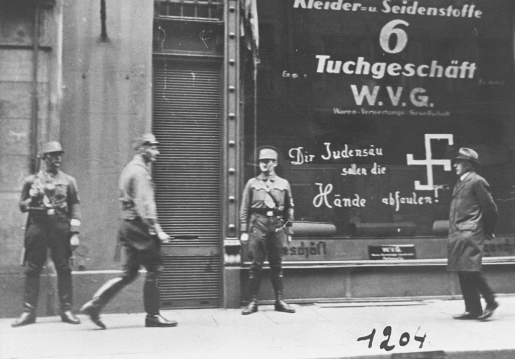 Shortly after the German annexation of Austria, Nazi Storm Troopers stand guard outside a Jewish-owned business.