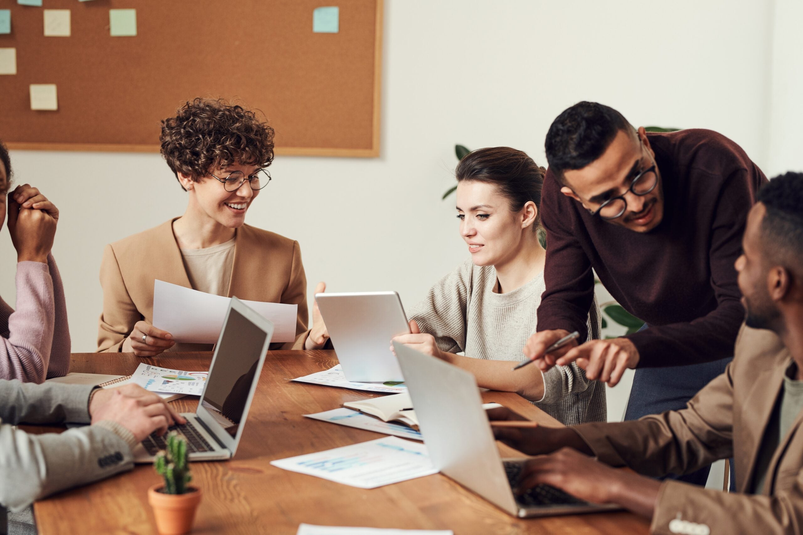 diverse group of people in a meeting space with laptops discussing something together