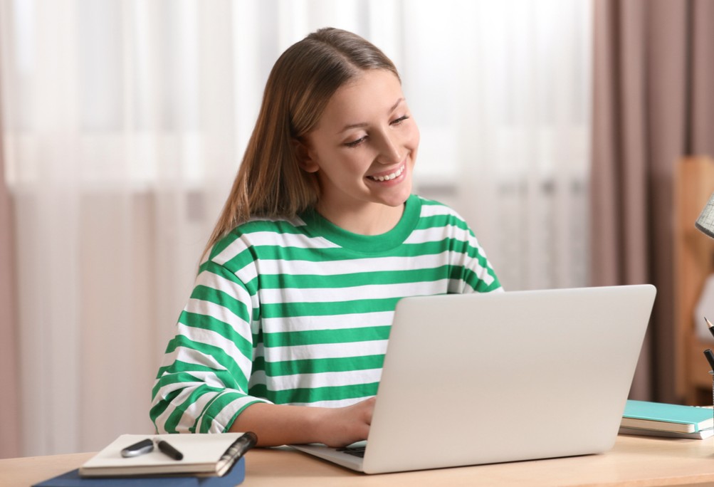 Estudante sorridente utilizando notebook para aprender como estudar por questões e aplicar o método de estudo reverso de forma eficiente.