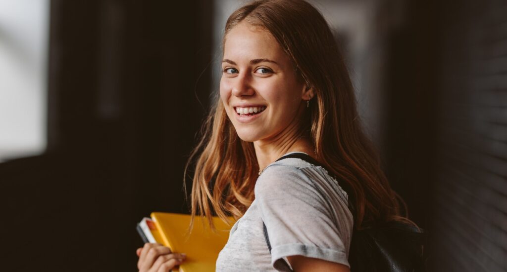 Estudante sorridente segurando cadernos, representando organização e motivação para seguir um plano de estudos eficaz.