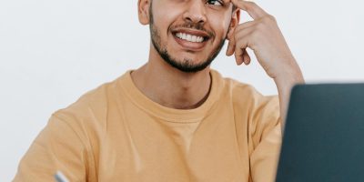 Estudante sorridente fazendo anotações e usando um laptop, representando a pesquisa sobre como funciona o SiSu, o Sistema de Seleção Unificada para ingresso em universidades públicas.