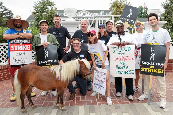 Colton Dunn, Adam Scott, Kirk Fox, Nick Offerman, Jim O’Heier, Aubrey Plaza, Alison Becker, Allan McLeod, Retta, Joe Mande, and Ben Schwartz alongside Lil Sebastian on a SAG-AFTRA picket line