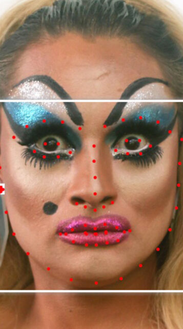 A white person with long, blonde hair, blue eyeshadow and pink lipstick with a white square framing their face with red facial recognition dots