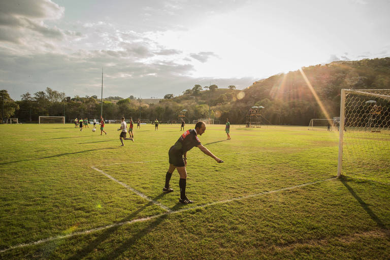 Atletas e juiz em campo de futebol; no céu, o sol brilha forte