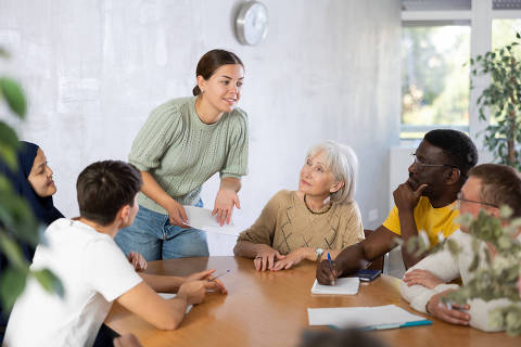 Smiling young girl participating in volunteer work discussing goals and objectives of project or event with group of associates, men and women of different ages and nationalities gathered around table 
( Foto:  JackF / adobe stock )