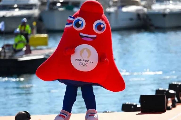 A imagem mostra a mascote das Olimpíadas de Paris 2024, vermelha, com um rosto sorridente