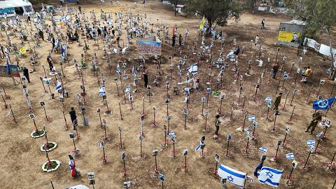 In this aerial view visitors walk around portraits of people who were taken hostage or killed in the Hamas attack on the Supernova music festival on October 7, at the site of the festival near Kibbutz Reim in southern Israel on May 13, 2024. (Photo by JACK GUEZ / AFP)