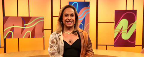 Cissa Guimarães (Sem Censura, TV Brasil) *** Local Caption *** Uma mulher sorridente está sentada em um estúdio com fundo laranja e painéis decorativos. Ela usa uma blusa preta e uma jaqueta com tons de marrom e cinza. O estúdio possui mesas de madeira em formato curvo e um ambiente iluminado. ORG XMIT: AGEN2402211555407394