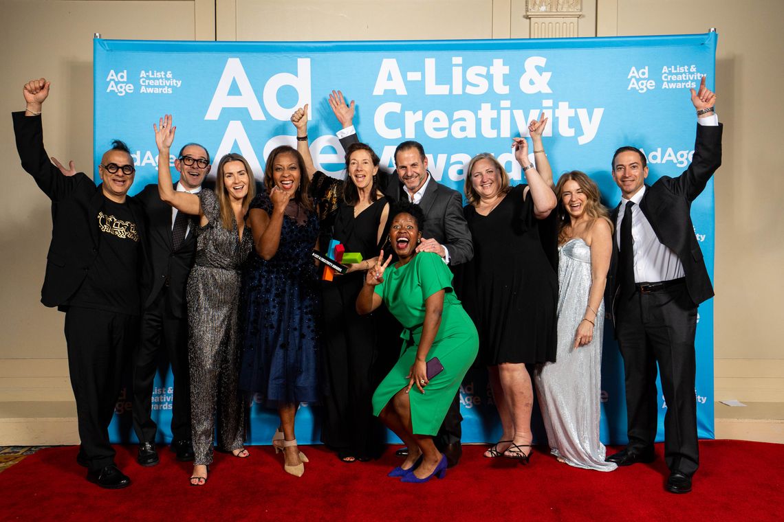 An image of ten people, with their arms raised in celebration, standing on a red carpet in front of a backdrop with the Ad Age A-List logo.