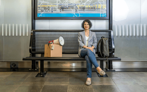 Mahnam Saeednia sits on a bench at the train station. Next to her is a package that points a megaphone at her.